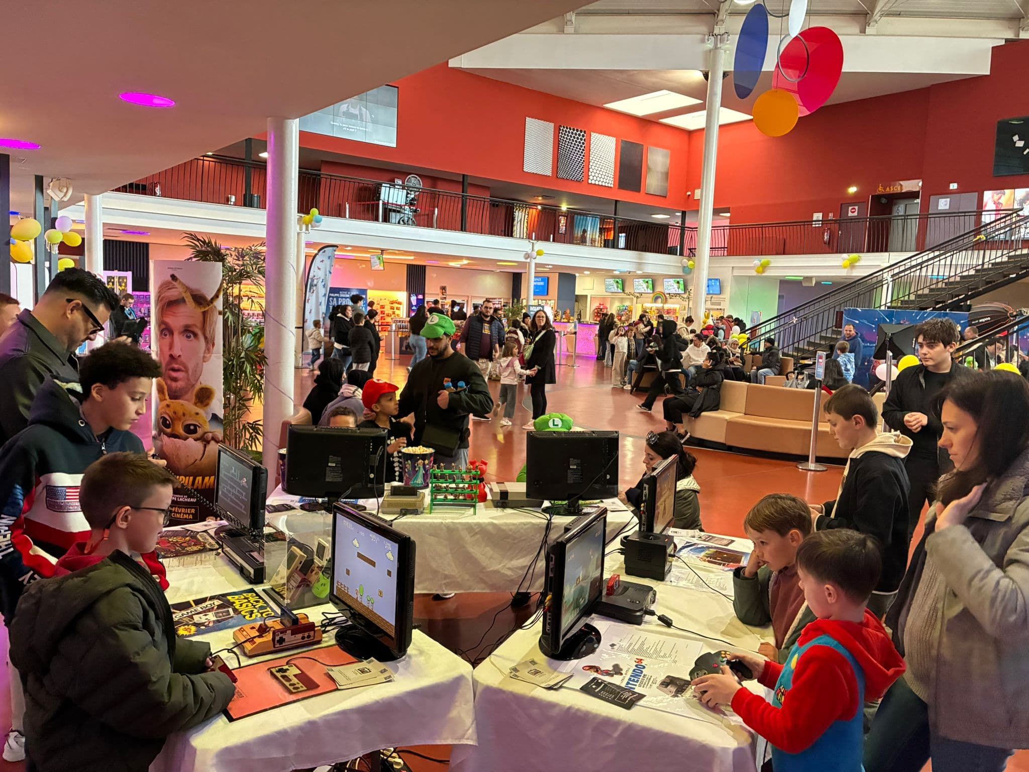 Animation rétro gaming du P'tit Comité : stand avec consoles et écrans installés dans un espace public, enfants et adultes qui jouent